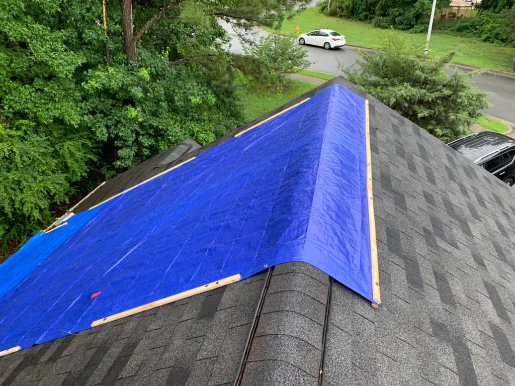 Blue emergency tarp secured over a section of storm-damaged shingle roofing